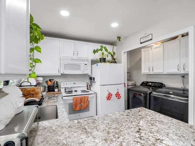 kitchen with white appliances, white cabinetry, light stone countertops, and washer and dryer