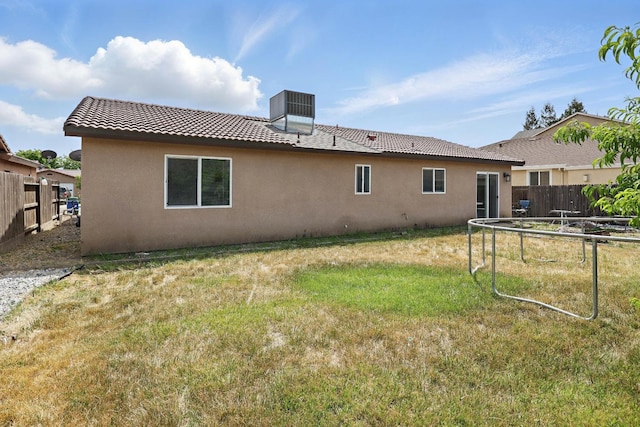 back of house with a tiled roof, a lawn, fence, and stucco siding