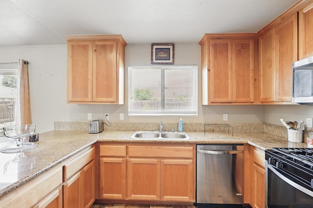 kitchen featuring light stone counters, a sink, appliances with stainless steel finishes, and a peninsula