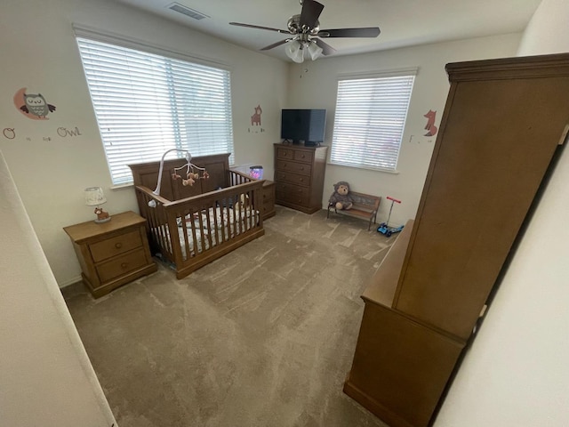 bedroom with visible vents, a nursery area, multiple windows, and light colored carpet