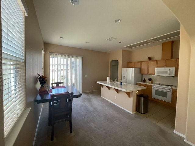 kitchen featuring white appliances, carpet flooring, an island with sink, and light countertops