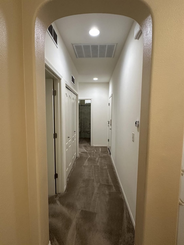 corridor with visible vents, arched walkways, baseboards, and dark carpet