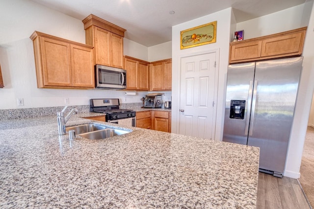 kitchen featuring light stone countertops, appliances with stainless steel finishes, a sink, light wood-style flooring, and a peninsula