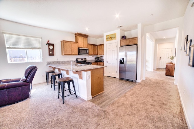 kitchen featuring a peninsula, a kitchen bar, light carpet, and stainless steel appliances