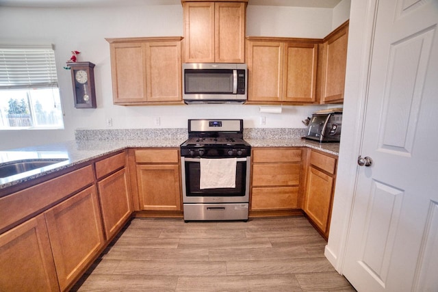kitchen featuring light stone counters, appliances with stainless steel finishes, and light wood-type flooring