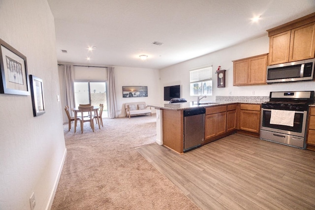 kitchen featuring brown cabinets, a sink, a peninsula, open floor plan, and stainless steel appliances