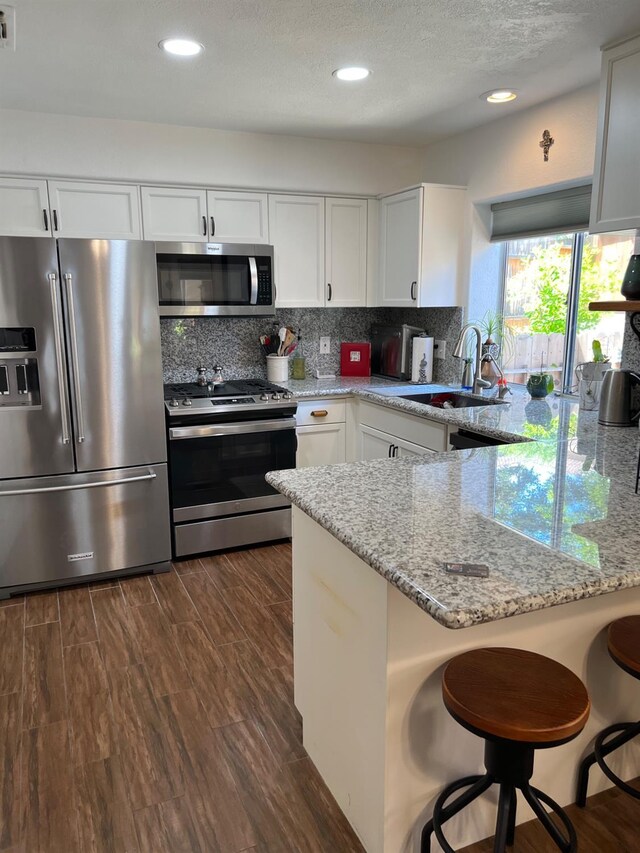 9552 N Whitehouse Dr, Fresno, CA 93720 - kitchen featuring appliances with stainless steel finishes, a sink, a peninsula, white cabinetry, and light stone countertops