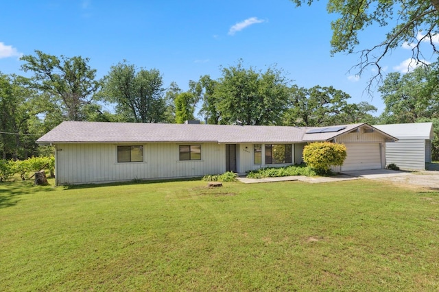 ranch-style house with a garage, a front lawn, driveway, and solar panels