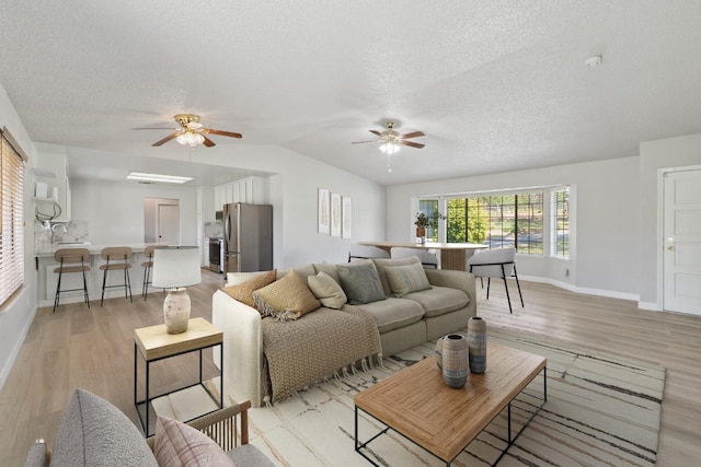 living area with a ceiling fan, light wood-type flooring, and a textured ceiling