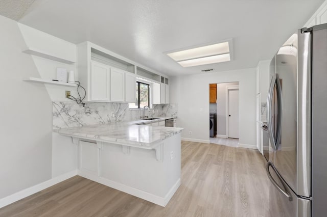 kitchen with a sink, a peninsula, stainless steel appliances, washer / dryer, and light wood-style floors