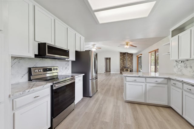 kitchen with light wood finished floors, white cabinetry, a peninsula, decorative backsplash, and appliances with stainless steel finishes