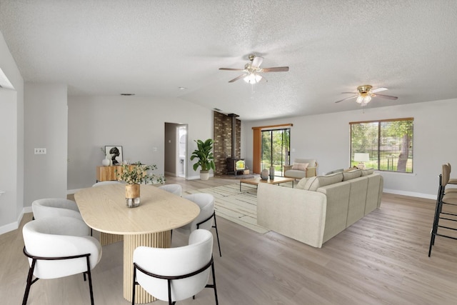 interior space with lofted ceiling, a wood stove, a textured ceiling, a ceiling fan, and light wood-style floors