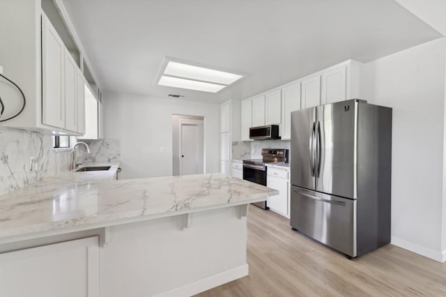 kitchen with a peninsula, light wood-style flooring, a sink, backsplash, and appliances with stainless steel finishes