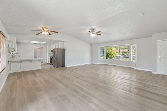 unfurnished living room featuring light wood-type flooring, ceiling fan, a textured ceiling, and vaulted ceiling