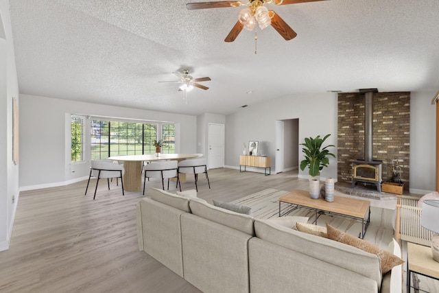 living area featuring light wood-style flooring, a textured ceiling, ceiling fan, a wood stove, and vaulted ceiling