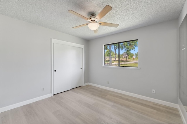 unfurnished bedroom with light wood finished floors, a textured ceiling, a closet, and baseboards