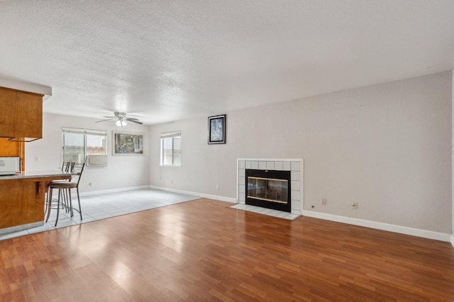 unfurnished living room featuring a fireplace, baseboards, ceiling fan, light wood-type flooring, and a textured ceiling