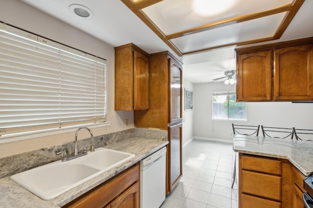kitchen with brown cabinets, white dishwasher, light tile patterned flooring, ceiling fan, and a sink
