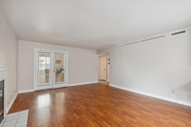 unfurnished living room with visible vents, light wood-style flooring, baseboards, and a tile fireplace