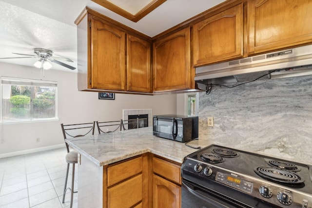 kitchen with a ceiling fan, baseboards, a peninsula, under cabinet range hood, and black appliances