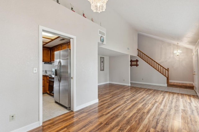 unfurnished living room featuring visible vents, baseboards, stairway, a chandelier, and light wood finished floors