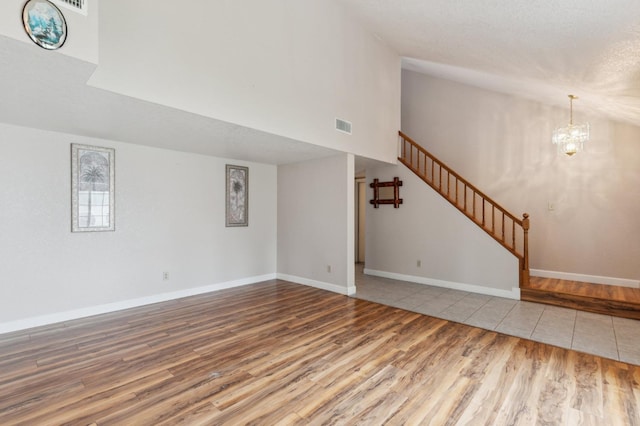 unfurnished living room featuring a towering ceiling, visible vents, wood finished floors, an inviting chandelier, and stairs
