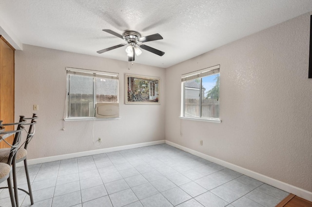 empty room with a textured wall, baseboards, ceiling fan, a textured ceiling, and light tile patterned floors