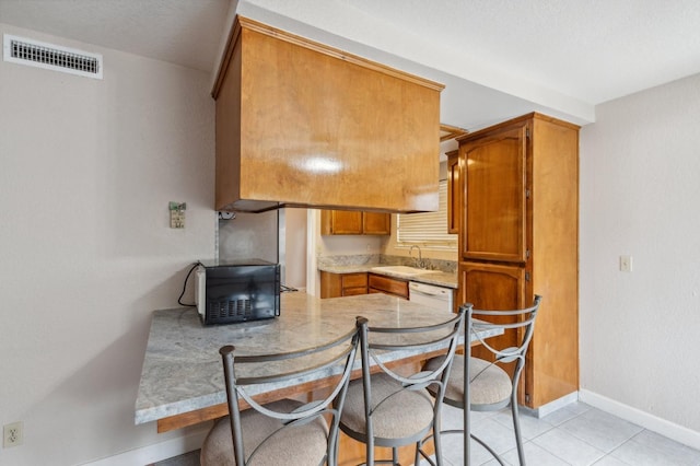 kitchen with visible vents, black microwave, baseboards, light countertops, and brown cabinets