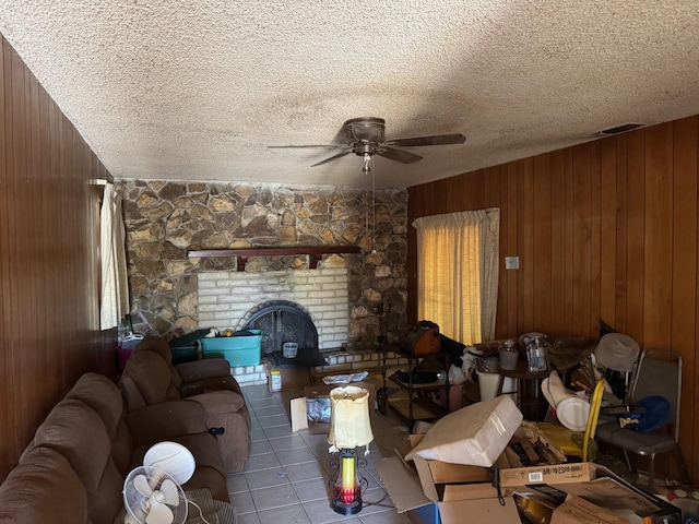 living room with ceiling fan, a textured ceiling, tile patterned flooring, a fireplace, and wood walls