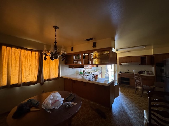 kitchen featuring visible vents, open shelves, a peninsula, a notable chandelier, and under cabinet range hood