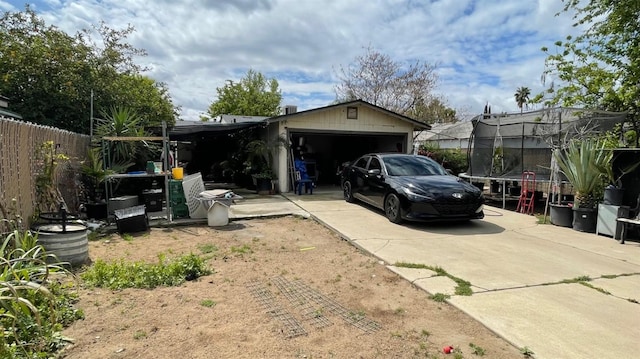 exterior space featuring a garage, a trampoline, fence, and concrete driveway