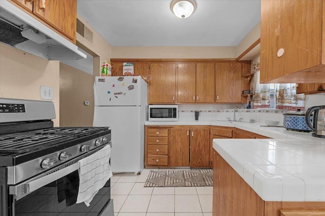 4185 E Turner Ave, Fresno, CA 93702 - kitchen featuring freestanding refrigerator, stainless steel gas stove, tile countertops, under cabinet range hood, and a sink