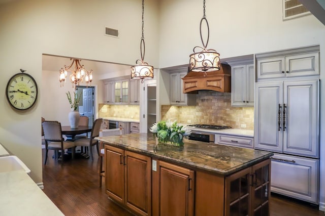 kitchen with backsplash, a towering ceiling, a kitchen island, visible vents, and dark wood-style floors