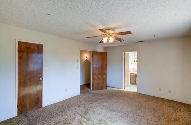 unfurnished bedroom featuring carpet, ensuite bath, a textured ceiling, and visible vents