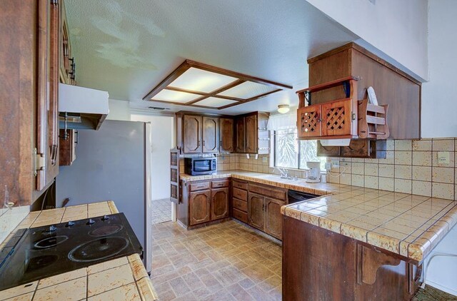 kitchen featuring decorative backsplash, stone finish floor, tile counters, black electric cooktop, and stainless steel microwave