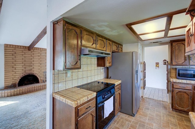 kitchen featuring a fireplace, stainless steel appliances, tile countertops, backsplash, and under cabinet range hood