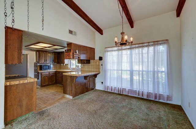 kitchen featuring brown cabinets, a notable chandelier, stainless steel appliances, a peninsula, and backsplash