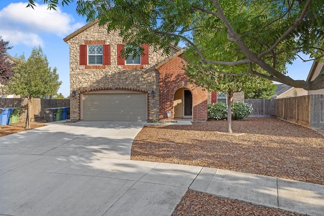 traditional-style house with fence, an attached garage, driveway, and stone siding
