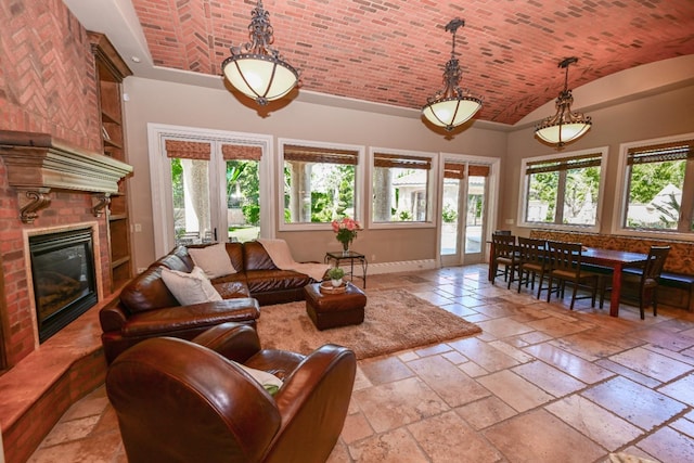 living area featuring baseboards, a fireplace, stone tile flooring, and lofted ceiling
