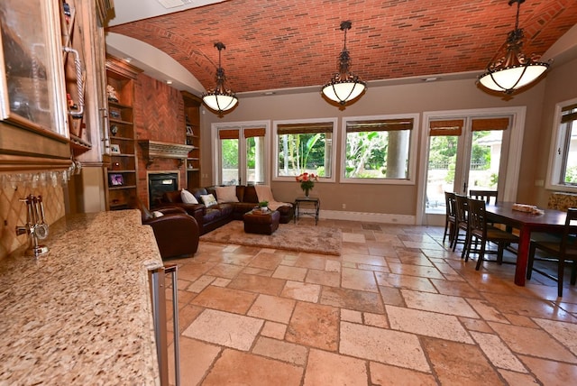 living room featuring a glass covered fireplace, built in shelves, stone tile floors, baseboards, and brick ceiling
