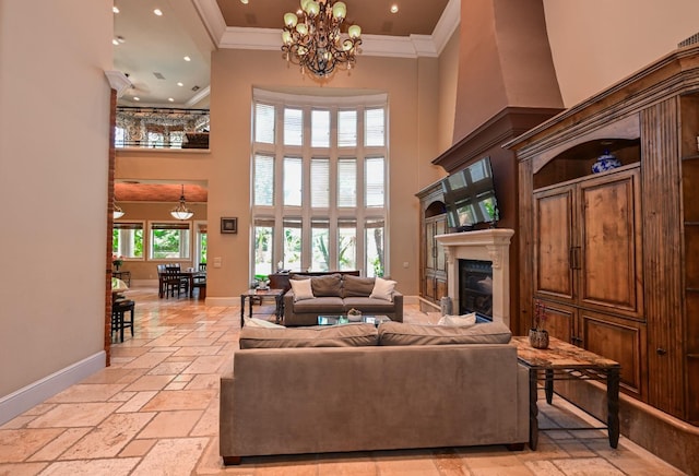 living area with a towering ceiling, crown molding, baseboards, a glass covered fireplace, and stone tile floors