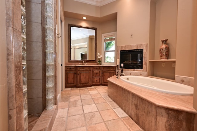 full bathroom with vanity, stone tile floors, a tile fireplace, ornamental molding, and a garden tub