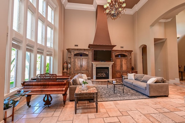 living area featuring a towering ceiling, arched walkways, a glass covered fireplace, ornamental molding, and stone tile floors