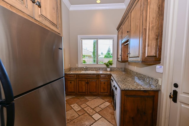 kitchen featuring brown cabinetry, stainless steel refrigerator, a sink, ornamental molding, and stone tile floors