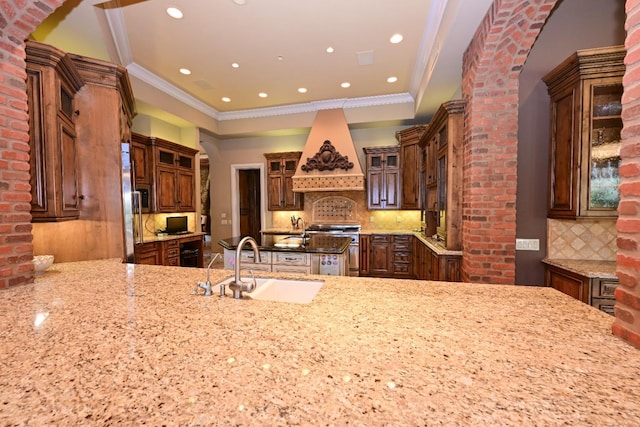 kitchen with light stone countertops, appliances with stainless steel finishes, a sink, custom range hood, and tasteful backsplash