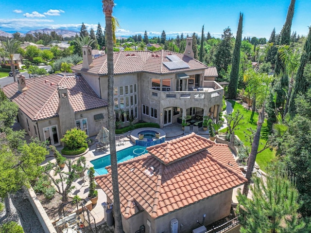 back of property featuring a chimney, a tile roof, a patio area, a balcony, and roof mounted solar panels