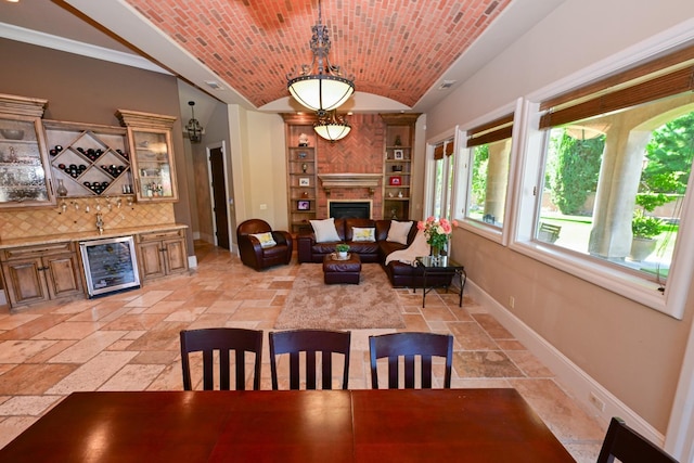 dining room featuring a dry bar, baseboards, lofted ceiling, wine cooler, and stone tile flooring