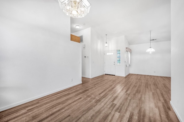 unfurnished living room featuring baseboards, wood finished floors, and a notable chandelier