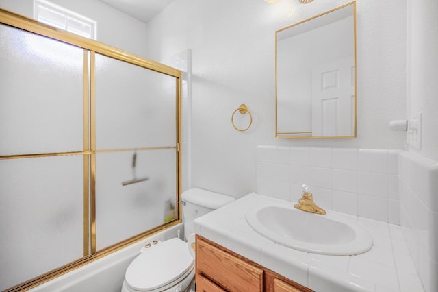 bathroom featuring backsplash, toilet, shower / bath combination with glass door, and vanity