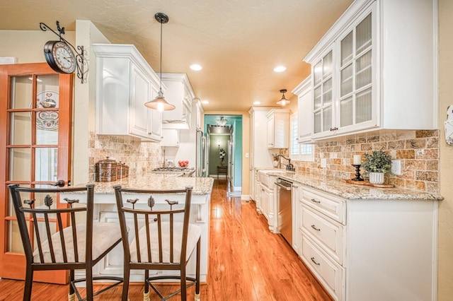 kitchen with glass insert cabinets, stainless steel dishwasher, white cabinets, a peninsula, and light wood-style floors